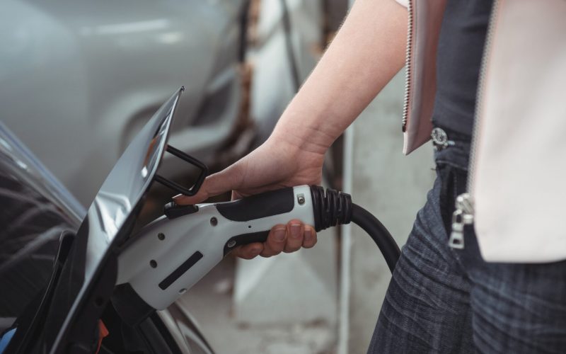 Mid section of woman using mobile phone while charging electric car at vehicle charging station