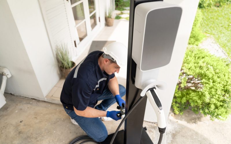 Qualified technician install home EV charging station, providing maintenance service for electric vehicle's battery charging platform at home. EV car technology for residential utilization. Synchronos